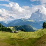 green grass field near mountains under white clouds and blue sky